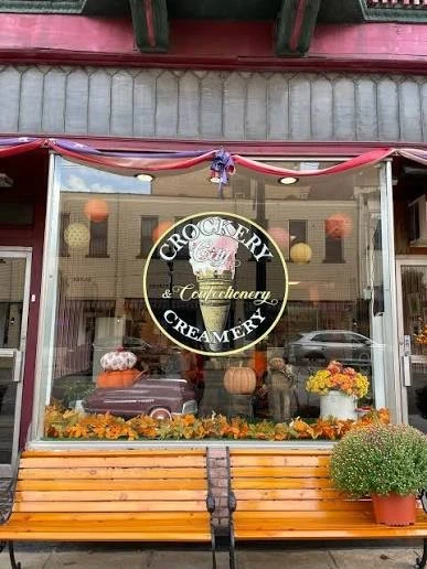 The Crockery City Creamery storefront window on Fifth Street, with the logo in the glass and a wooden bench out front
